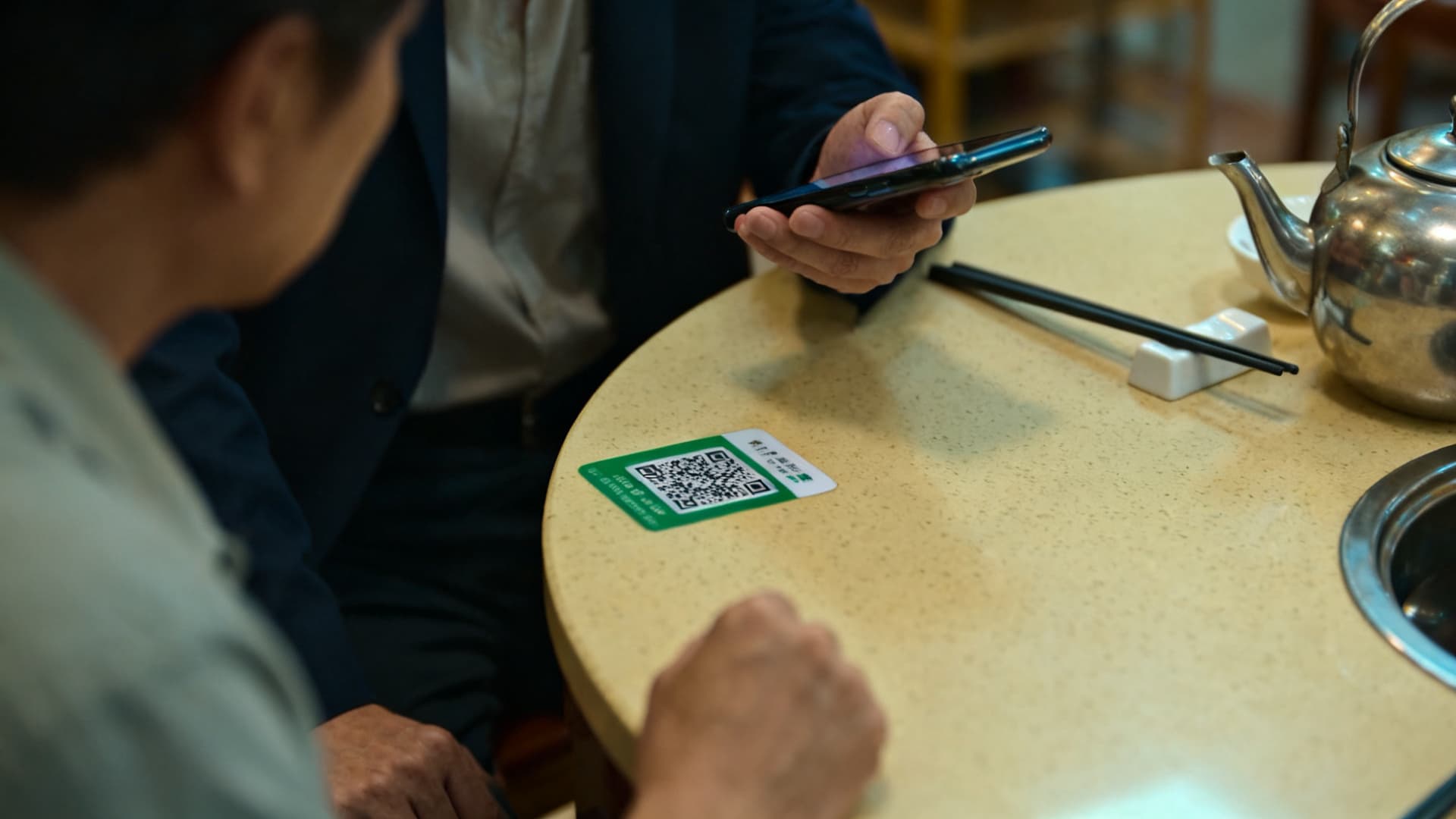 фото: столик с наклейкой QR-кода, телефон над ней и палочки в подставке